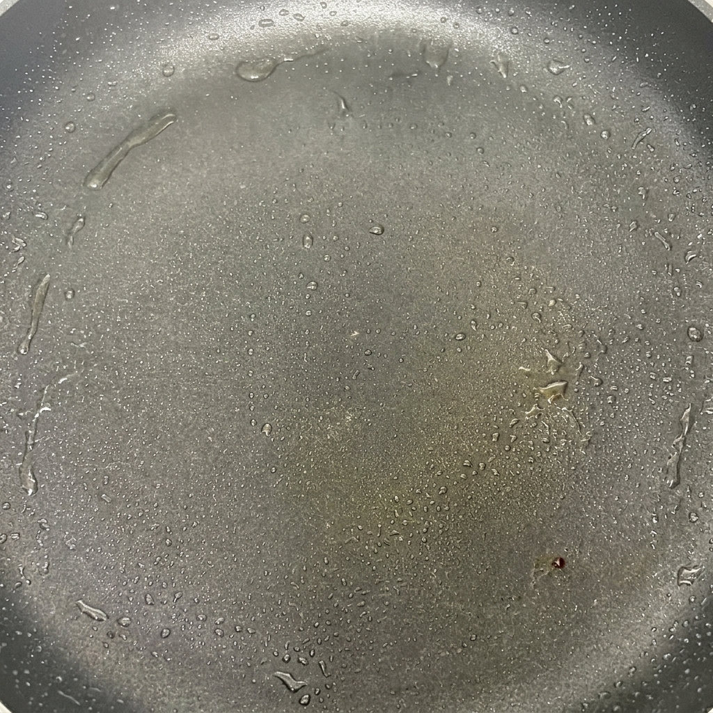 Sombreros de champiñón chisporroteando en una sartén caliente con aceite, comenzando a dorarse ligeramente.