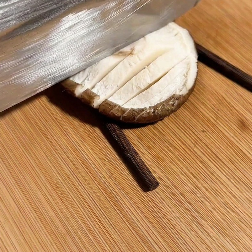 Un cuchillo cortando un patrón de cuadrícula en un champiñón colocado entre dos palillos.