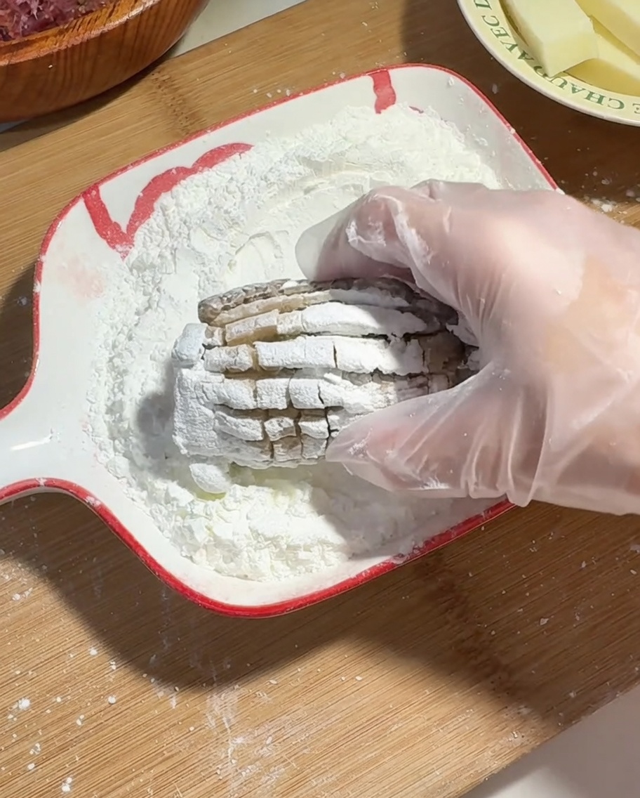 Una mano con guante de plástico cubriendo un champiñón shiitake relleno de carne y queso con almidón de maíz.