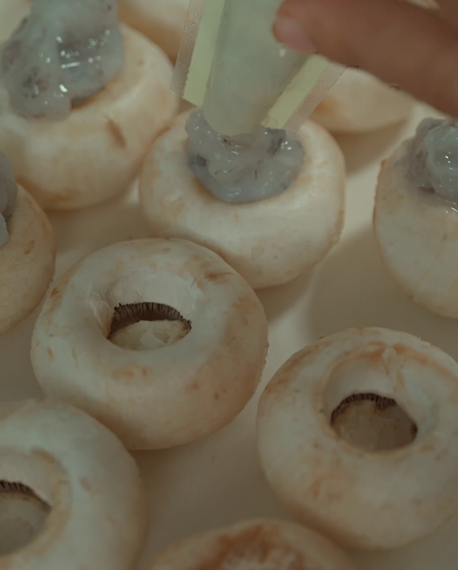 Pasta de camarones siendo introducida con una manga pastelera en el centro de los champiñones cocidos.