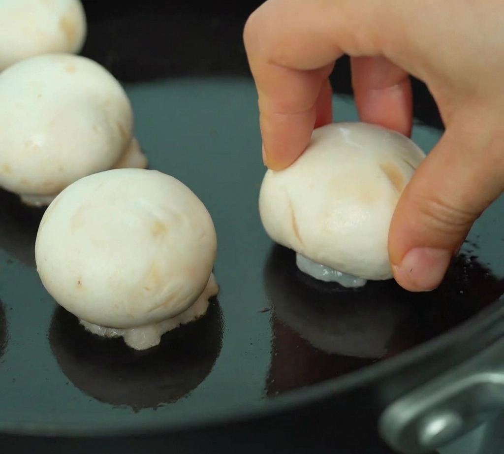 Champiñones rellenos sellándose en una sartén con el lado del camarón hacia abajo.
