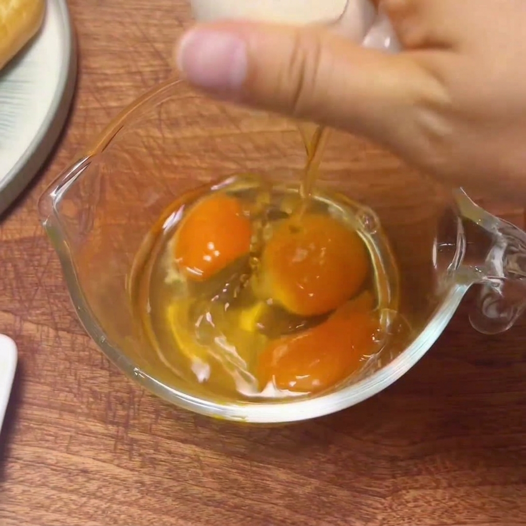 Huevos frescos rompiéndose en una jarra medidora de cristal, listos para ser batidos.