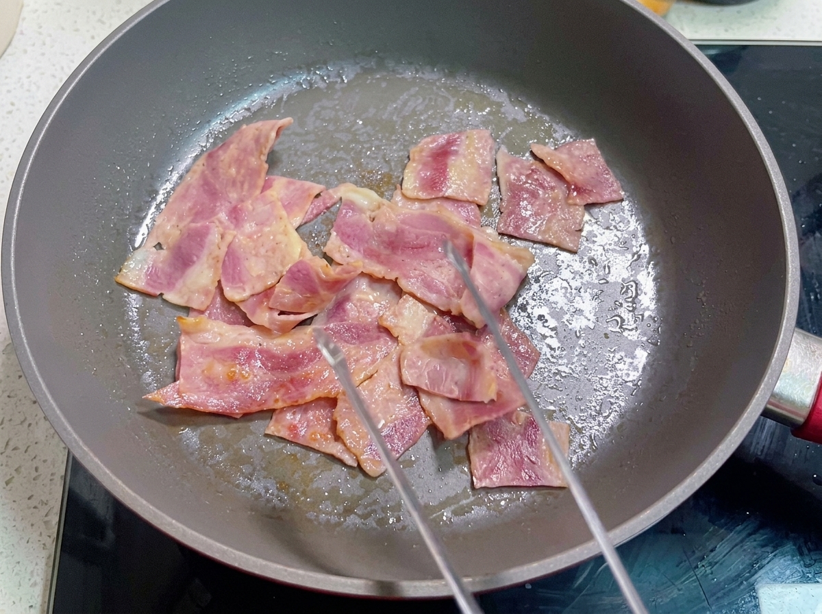 Una sartén con beicon cocinado y la mezcla de huevo batido vertiéndose sobre él.