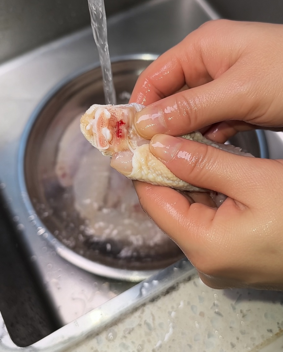 Primer plano de manos exprimiendo una alita de pollo cruda para expulsar la sangre de la articulación.