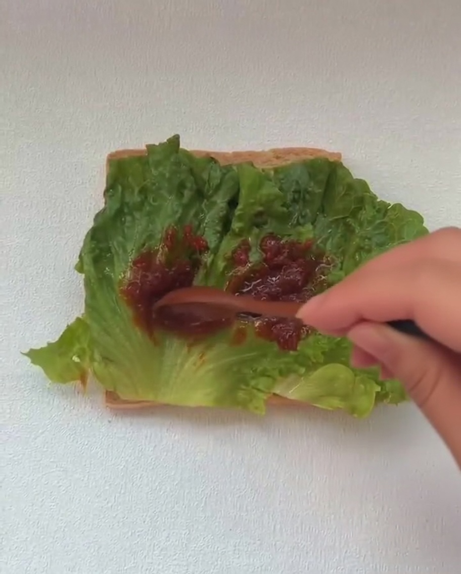 Un huevo frito recién cocinado siendo añadido al armado del sándwich, sobre una capa de lechuga verde.