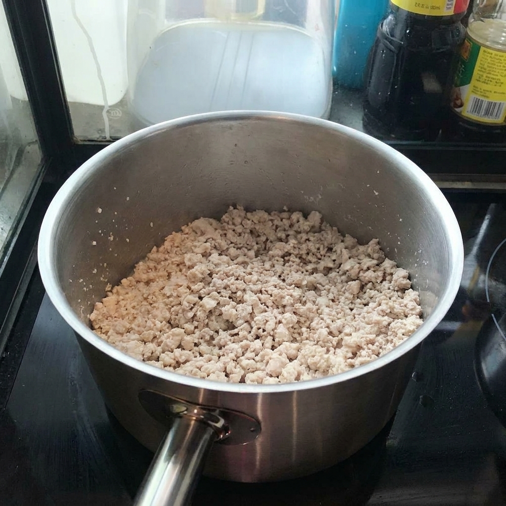 Cerdo picado dorándose en una olla de acero inoxidable mientras se remueve con una espátula.
