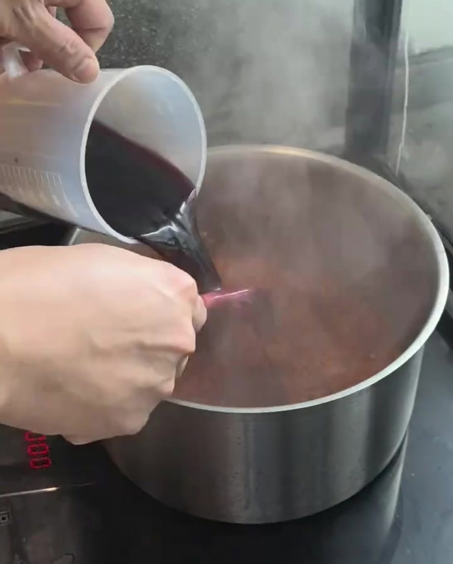 Vino tinto siendo vertido desde una taza medidora a la olla con los vegetales.