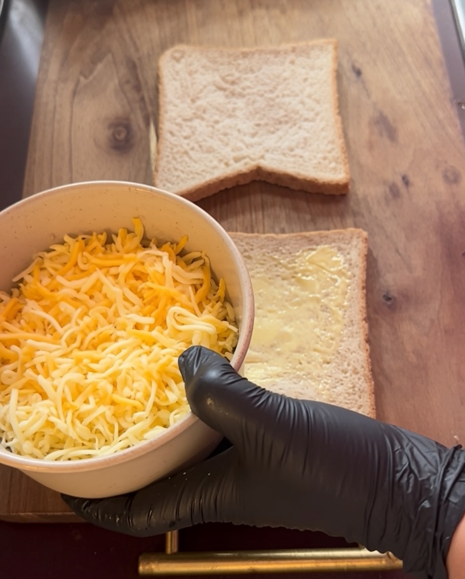 Queso rallado siendo distribuido sobre las rebanadas de pan con mantequilla.