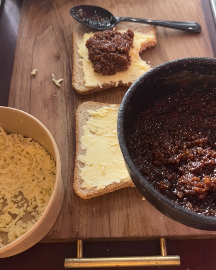 Una porción generosa de salsa de carne siendo extendida sobre la capa de queso en el pan.