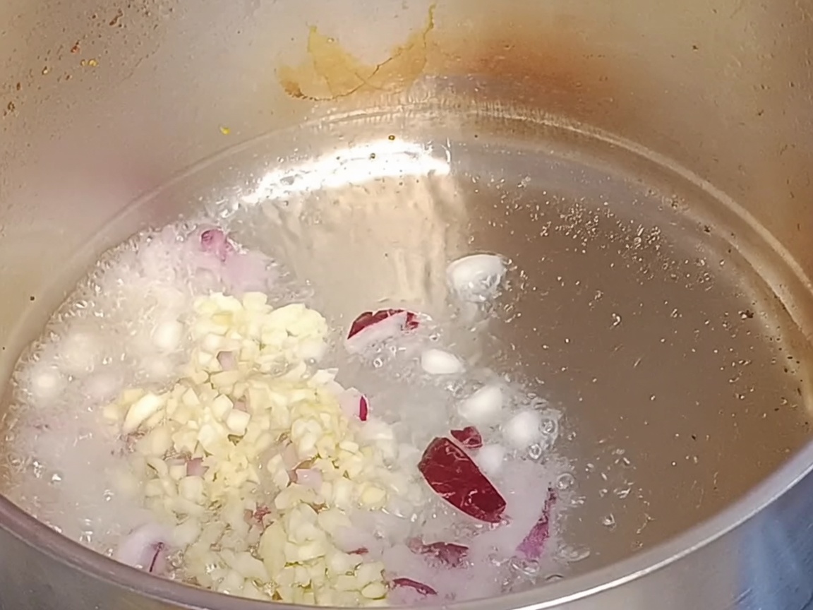 Cebollas rojas picadas y ajo picado sofriéndose en aceite caliente dentro de una olla de metal.