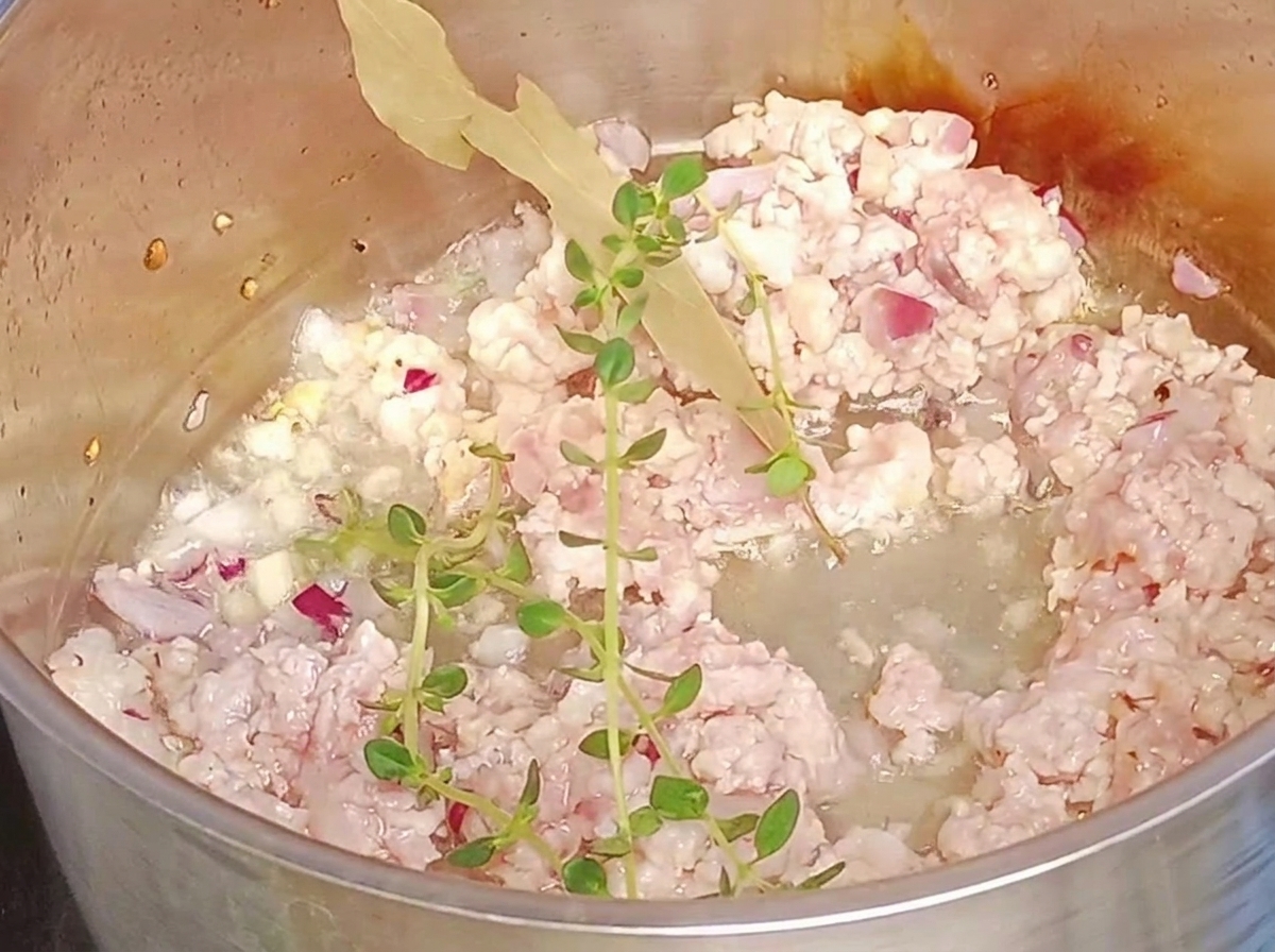 Ramas de tomillo fresco y una hoja de laurel añadidas a la carne molida en una olla.