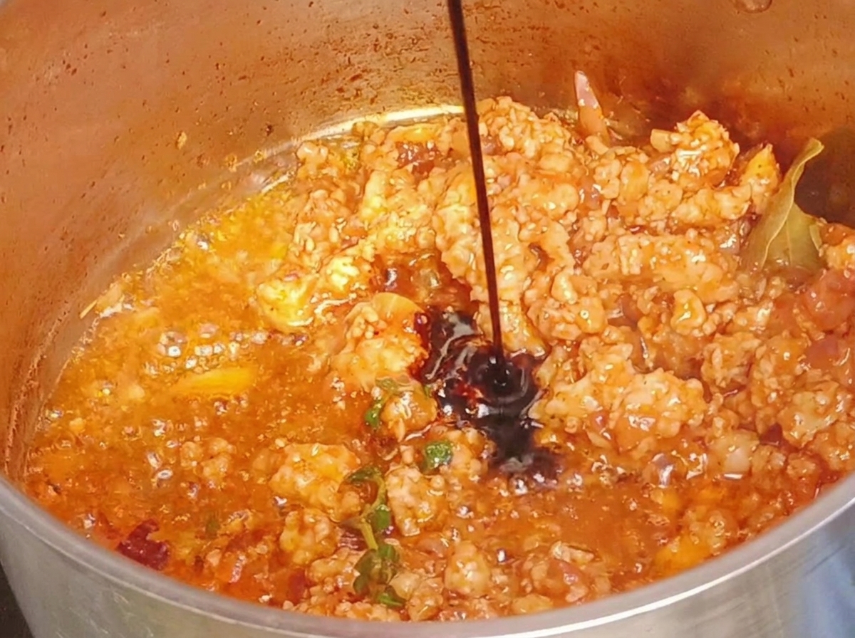 Salsa de soja oscura siendo vertida en una olla de carne molida cocinada.