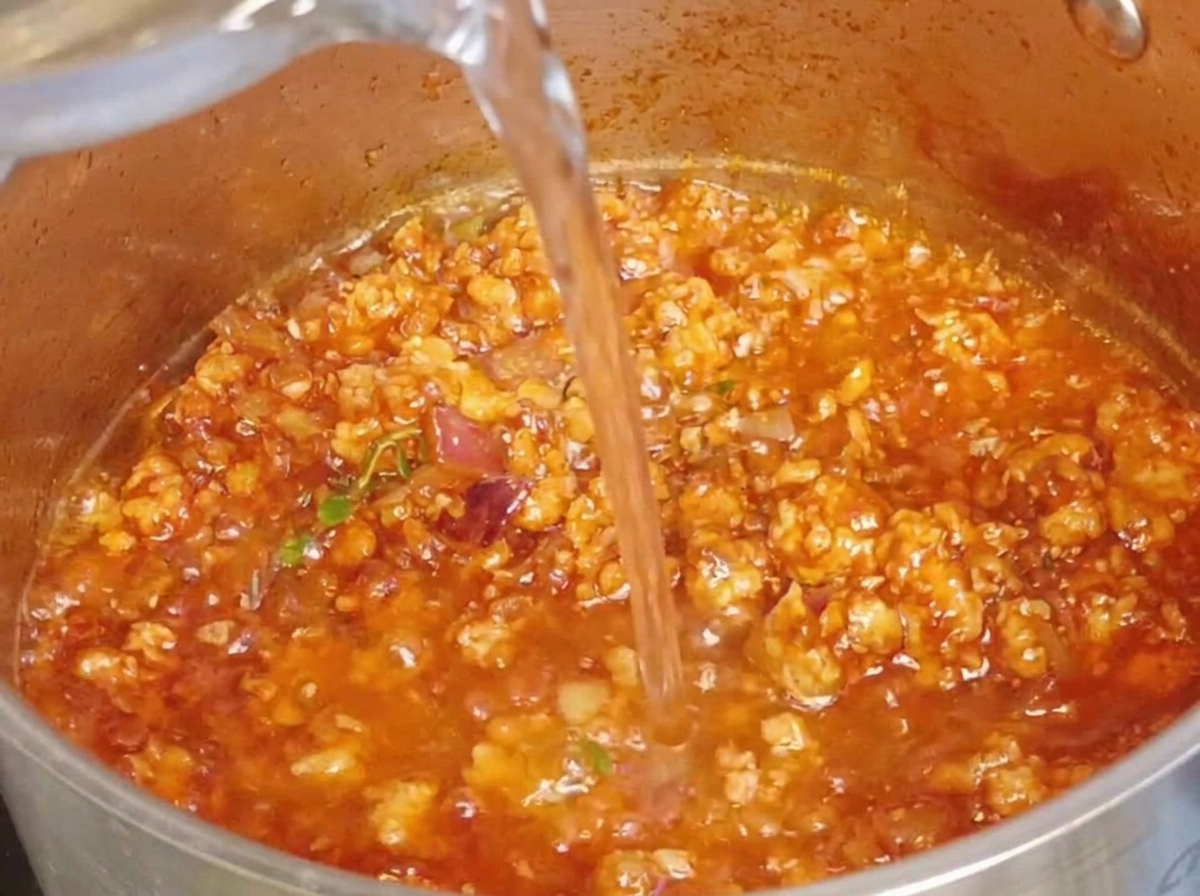 Agua clara siendo vertida en una olla que contiene la rica salsa de carne.