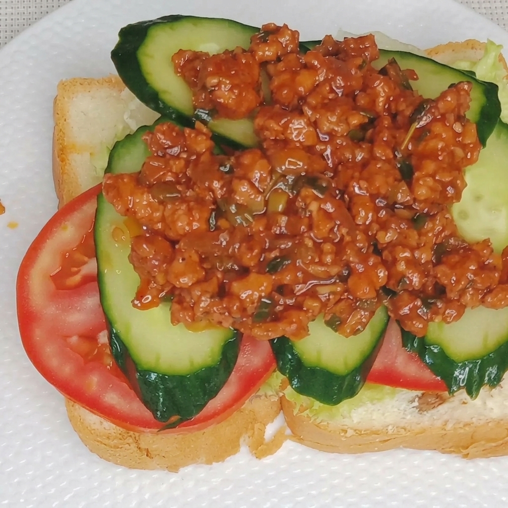 Primer plano de salsa cremosa de yema de huevo siendo rociada sobre una capa de salsa de carne en un sándwich.