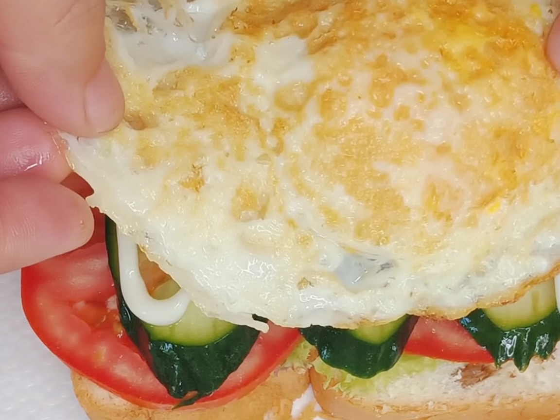 Un huevo frito perfecto siendo colocado sobre las capas ensambladas del sándwich.