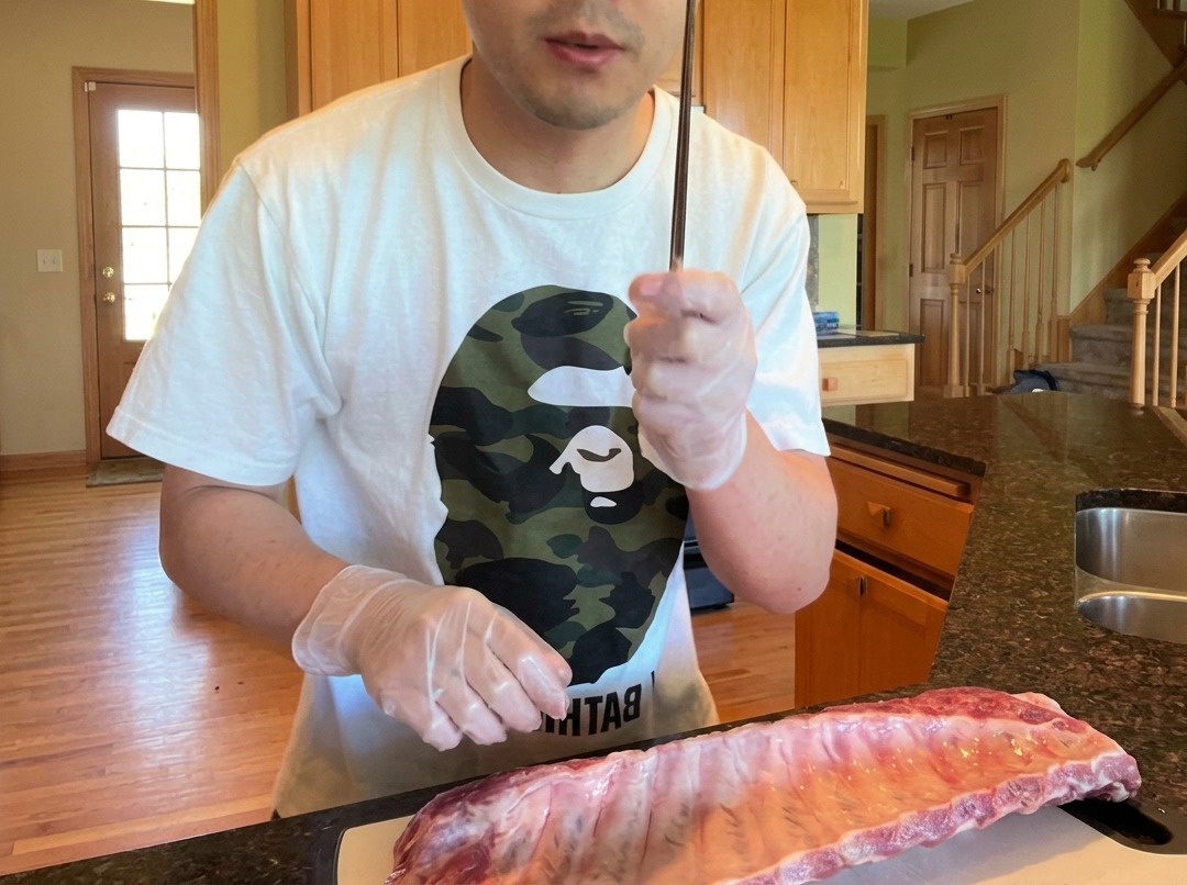 Primer plano de un palillo levantando la membrana de la parte posterior de una pieza de costillas de cerdo crudas.