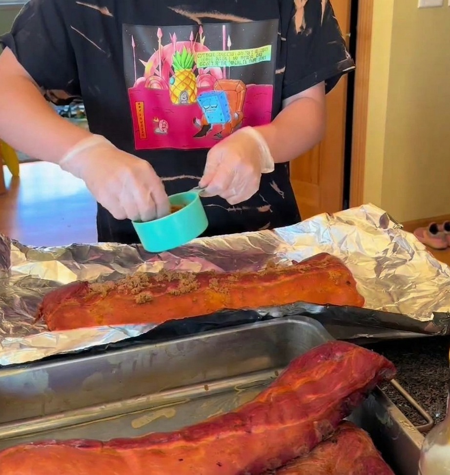 Costillas ahumadas sobre papel aluminio siendo sazonadas con un aliño seco y rociadas con miel.