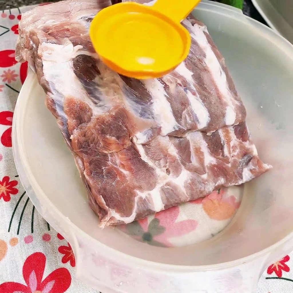 Salsa de ostras oscura siendo vertida sobre costillas de cerdo crudas en un cuenco blanco.