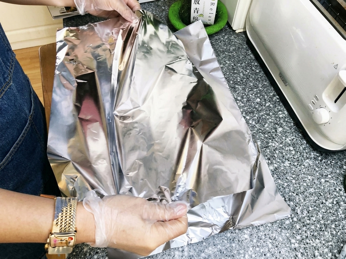 Manos doblando papel aluminio apretadamente sobre costillas de cerdo marinadas para crear un paquete sellado.