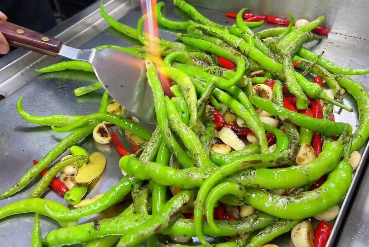 Dientes de ajo y chiles rojos siendo quemados en una plancha caliente con la llama de un soplete.