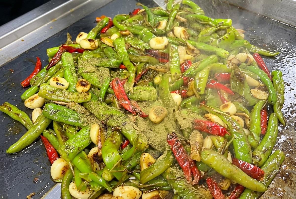 Condimentos y salsas añadidos sobre los chiles carbonizados en la plancha.
