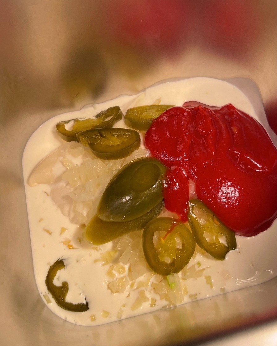 Salsa picante mexicana siendo vertida en un recipiente de metal que ya contiene la base de crema y mayonesa.