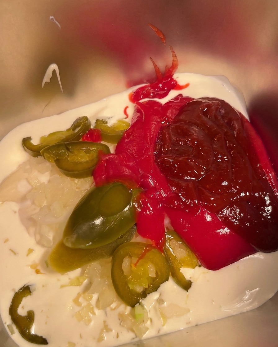 Chile en polvo siendo espolvoreado sobre la mezcla de mayonesa, crema y salsa picante en un recipiente de metal.
