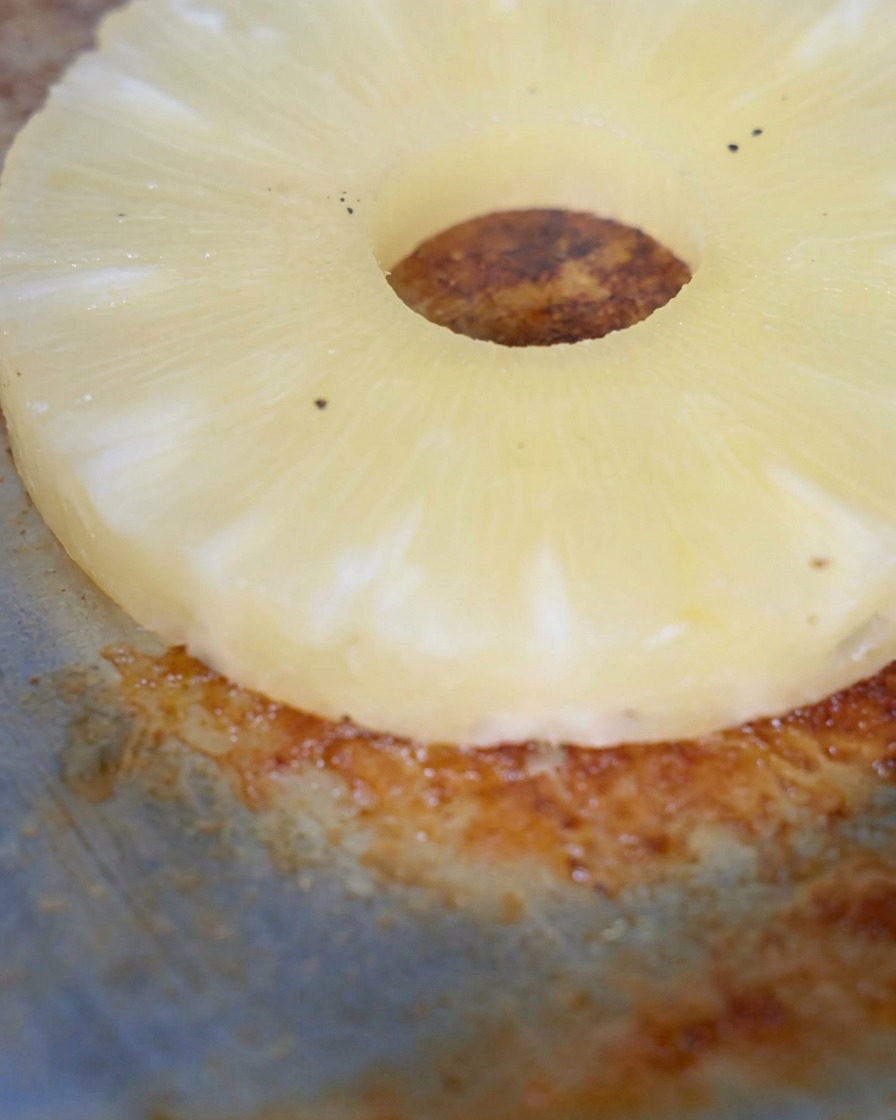 Una rodaja de piña asándose en la superficie caliente de una plancha oscura.