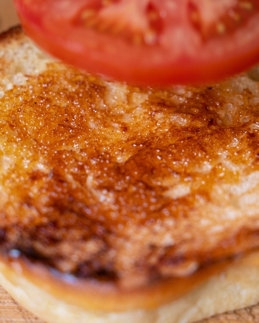 Una rodaja de tomate fresco siendo colocada sobre la base del pan tostado.