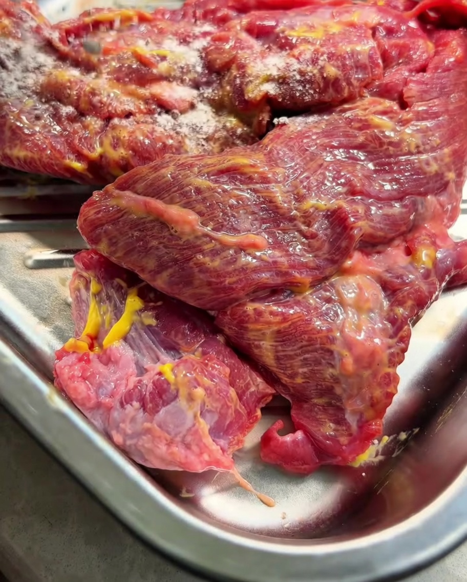 El pecho de res cubierto de mostaza en una bandeja de metal, con el sazonador seco en polvo espolvoreado por encima.