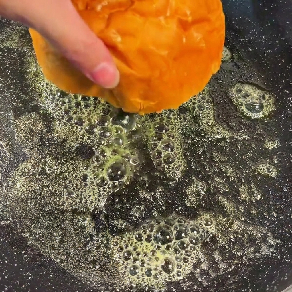 Mitades de pan de hamburguesa boca abajo en una sartén con mantequilla derretida, tostándose hasta adquirir un color dorado.