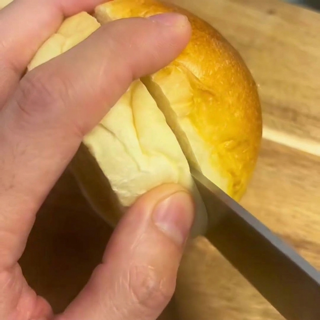 Un cuchillo cortando un pan de hamburguesa por la mitad sobre una tabla de madera.