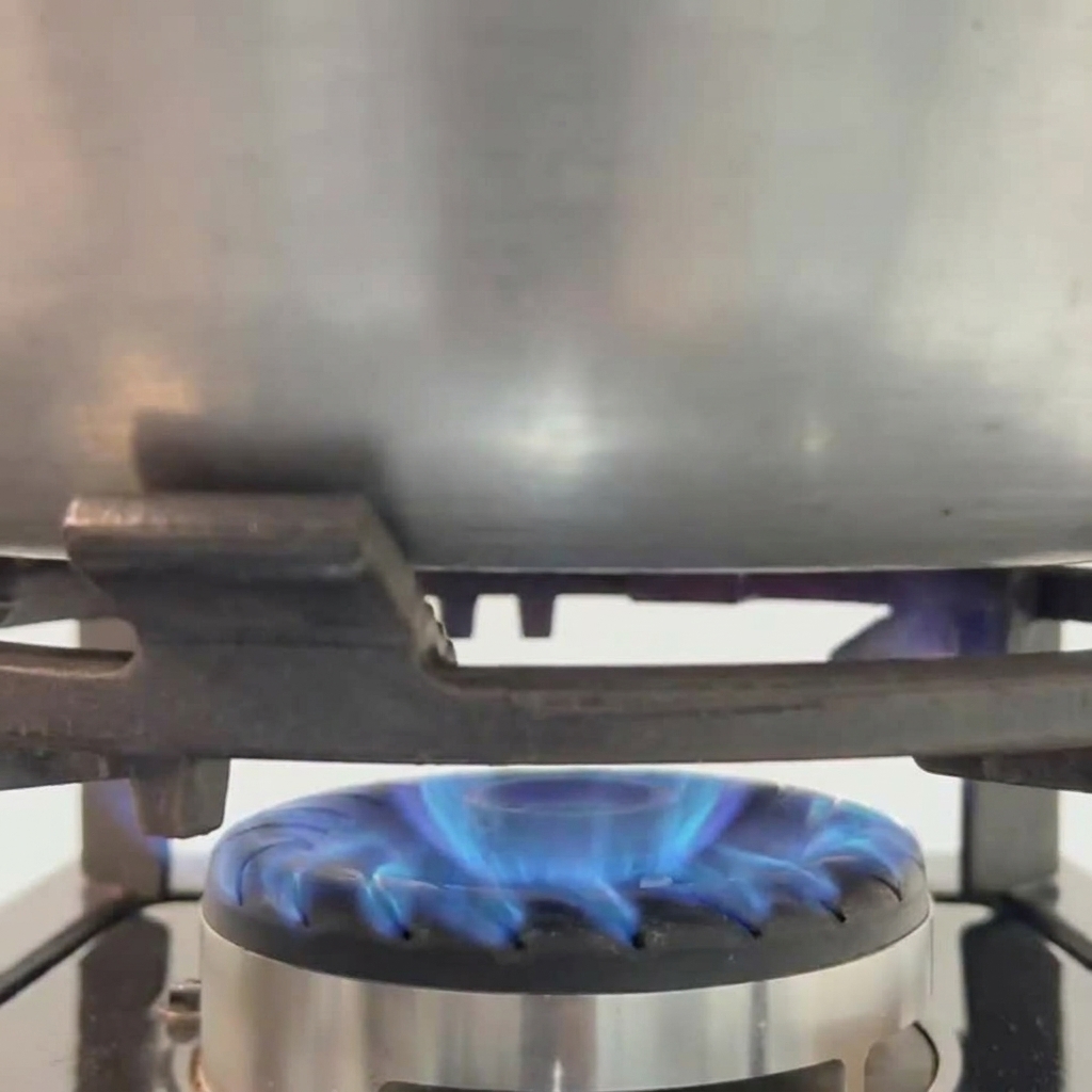 Una hamburguesa de carne friéndose en una sartén caliente mientras se sazona con sal y pimienta.