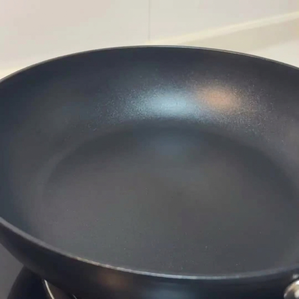 Champiñones laminados friéndose en una sartén y sazonados con sal y pimienta.