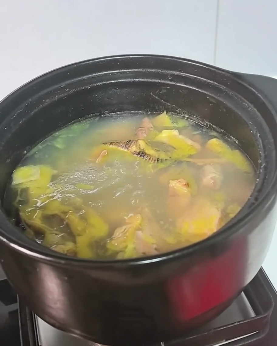 Una olla negra con sopa de pollo hirviendo a fuego lento sobre la hornilla.