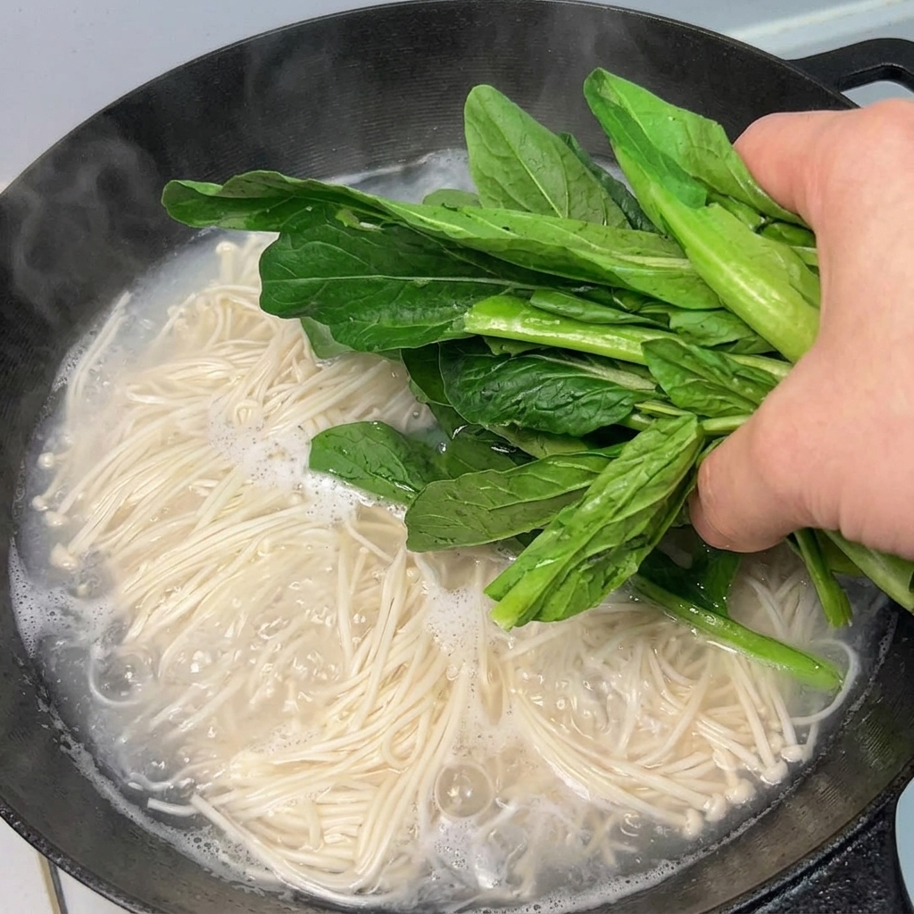 Verduras de hoja verde añadidas a la olla con fideos hirviendo.