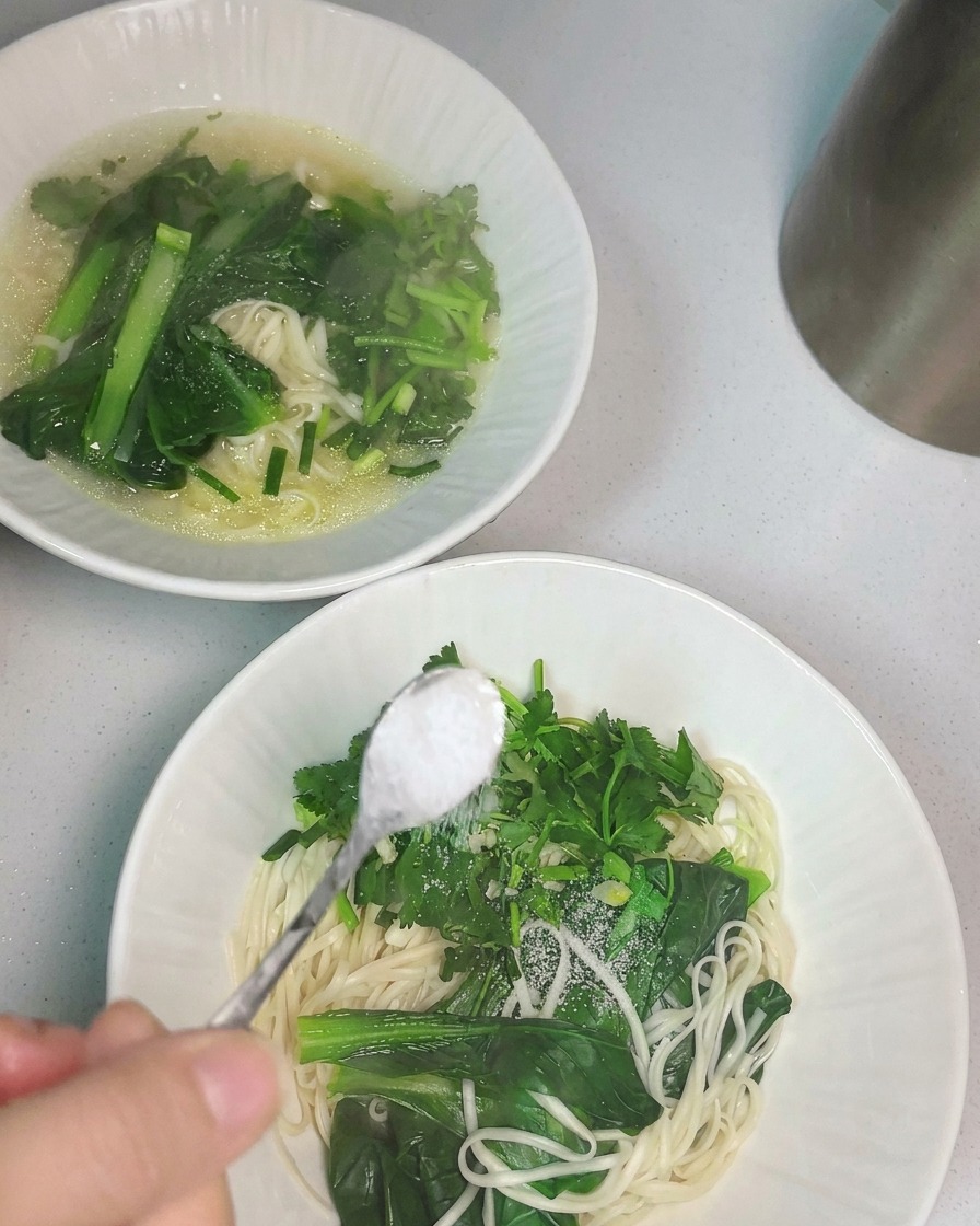 Caldo de pollo caliente siendo vertido con un cucharón sobre un tazón de fideos.