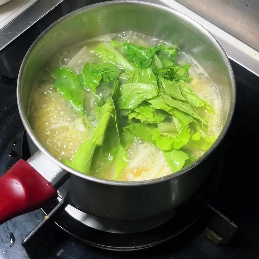 Verduras de hoja verde fresca añadiéndose a una olla de sopa de fideos hirviendo.