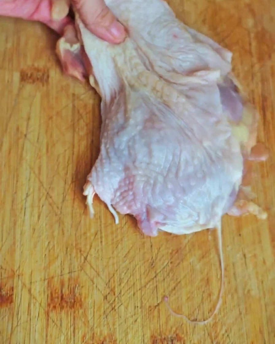 Primer plano de carne de muslo de pollo cortada en trozos pequeños sobre una tabla de madera.