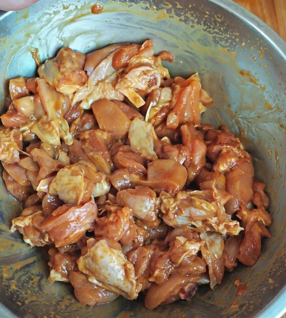 Trozos de pollo sazonados marinándose en un bol de metal, cubiertos con una mezcla de salsa brillante.