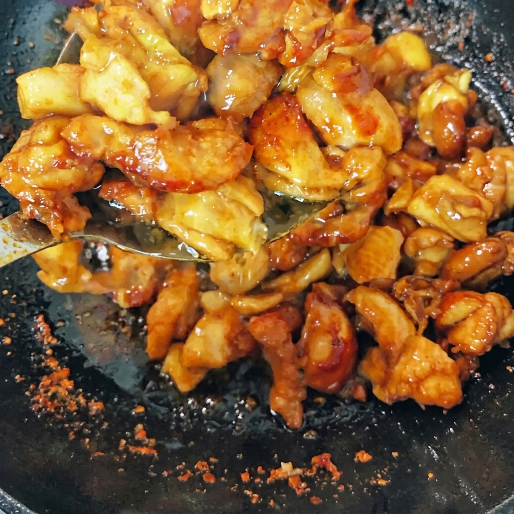 Trozos de pollo dorados salteándose en un wok con cebollino, rodajas de jengibre y chiles secos.