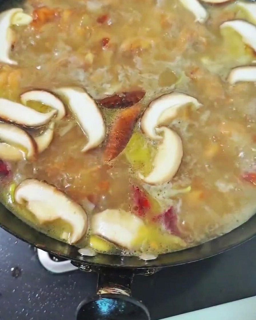 Setas shiitake en rodajas hirviendo en el caldo de pollo dentro del wok.