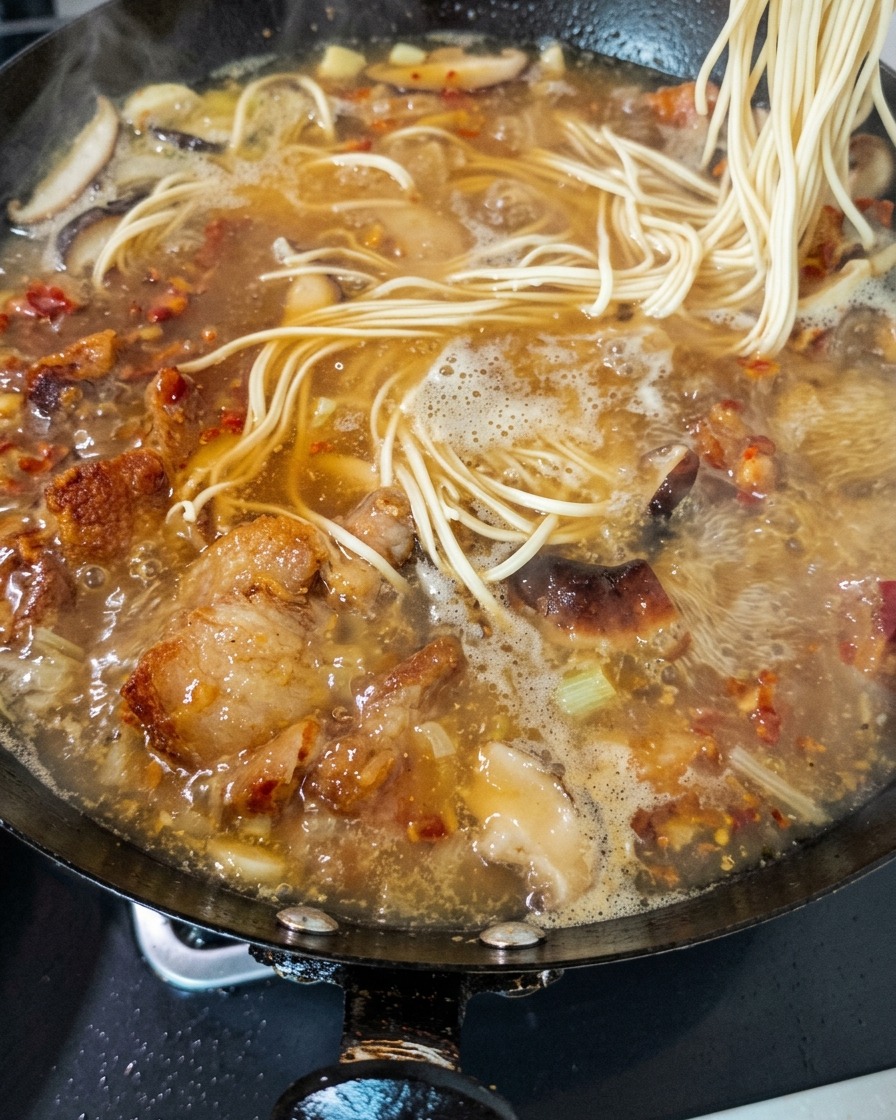 Fideos frescos siendo introducidos en un caldo rico y burbujeante de pollo y setas en un wok.