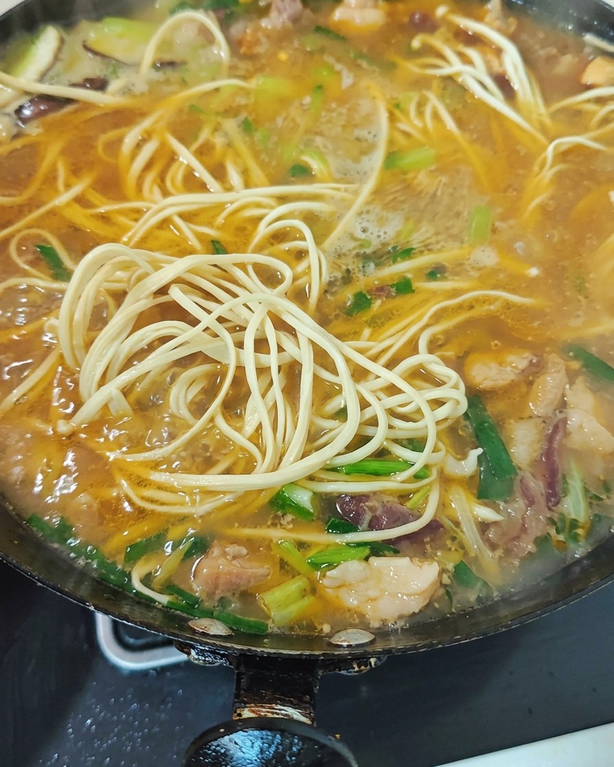 Vegetales verdes y brotes de ajo picados siendo mezclados en la sopa de fideos hirviendo.