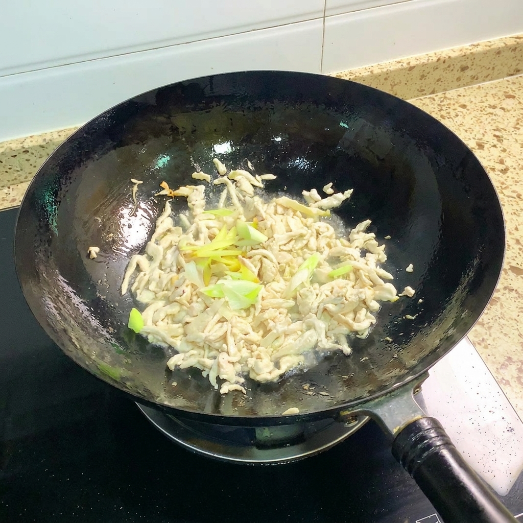 Cebolletas y jengibre siendo salteados con pollo cocinado en un wok.