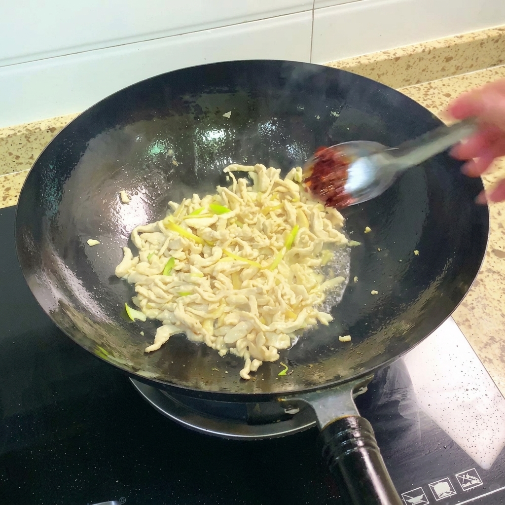 Pasta de judías Pixian siendo añadida al wok y mezclada con el pollo.
