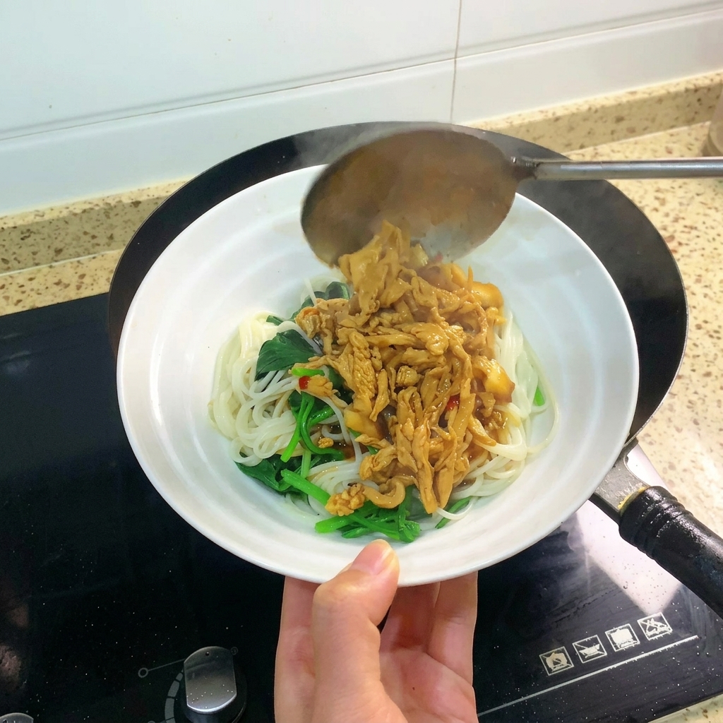 Un cucharón vertiendo una porción generosa de pollo desmenuzado braseado y salsa sobre un bol que contiene fideos y verduras de hoja verde.