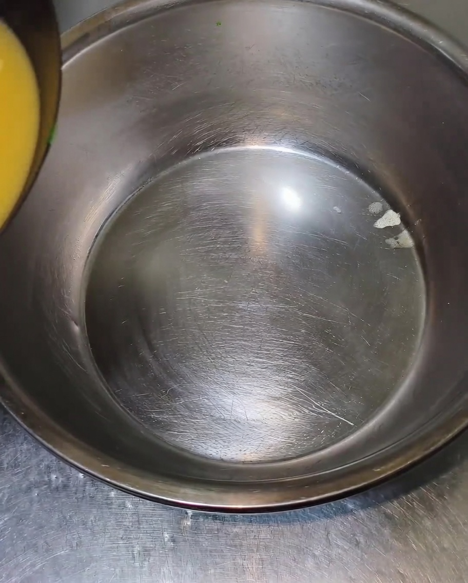 Caldo caliente vertiéndose desde el borde de un wok hacia un gran bol de mezcla de acero inoxidable.