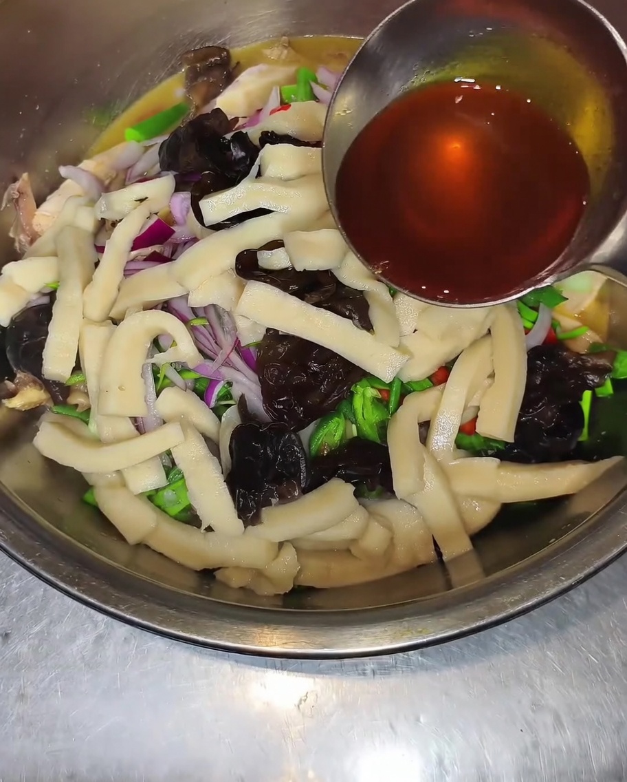 Primer plano de un cucharón rociando aceite de chile y pimienta sobre un bol con pollo, hongos, cebollas y pimientos.