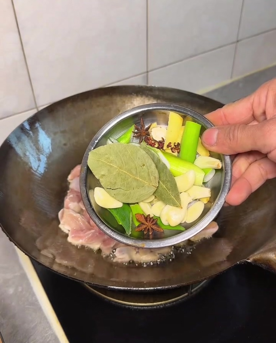 Una variedad de especias enteras siendo añadidas al pollo en el wok.